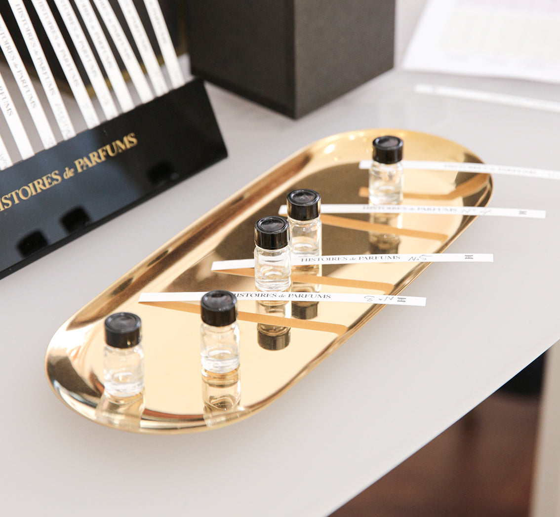 Gold tray with small perfume bottles and blotters on a white surface.