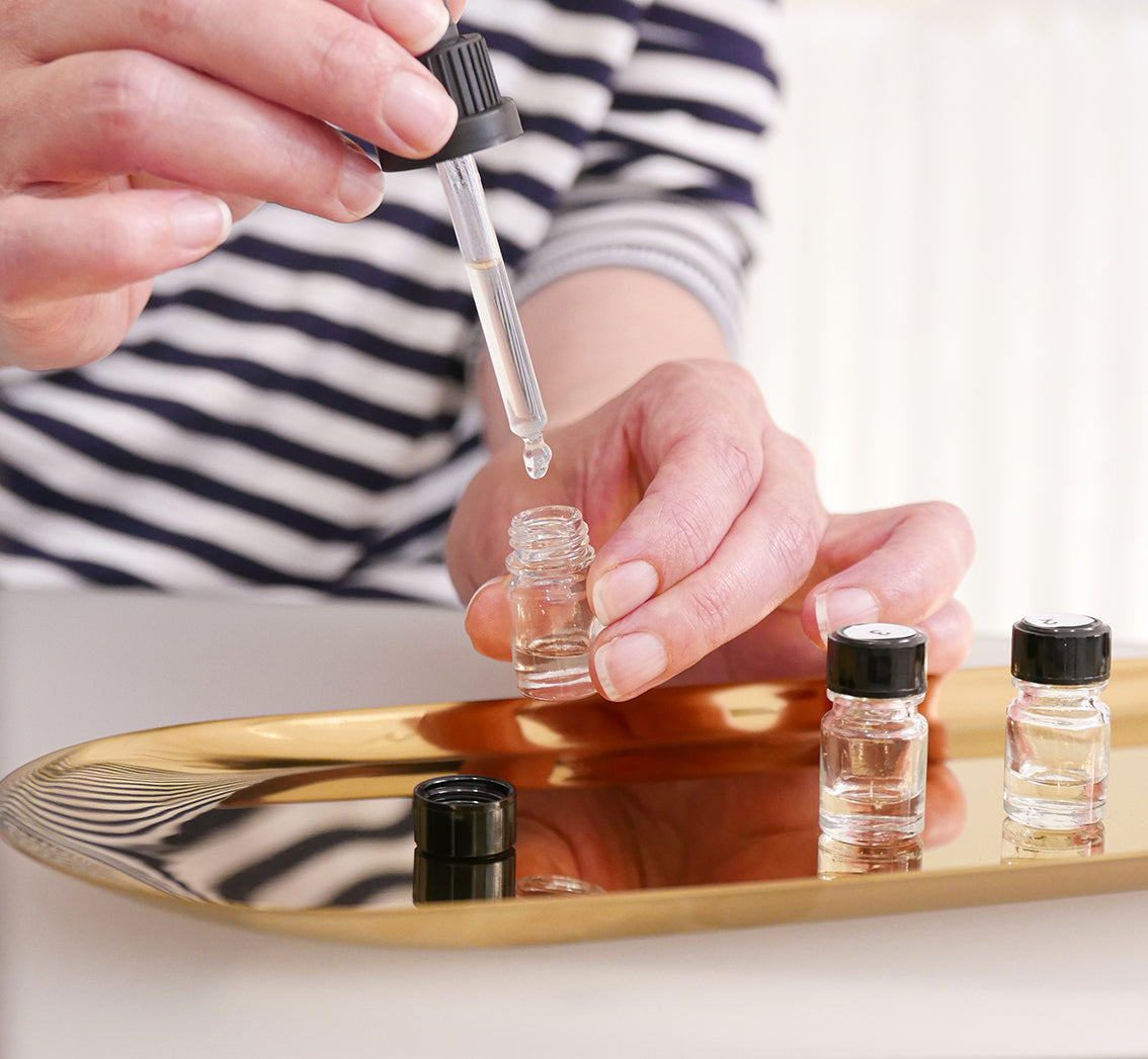 Person using a dropper to add liquid to small bottles on a gold tray.